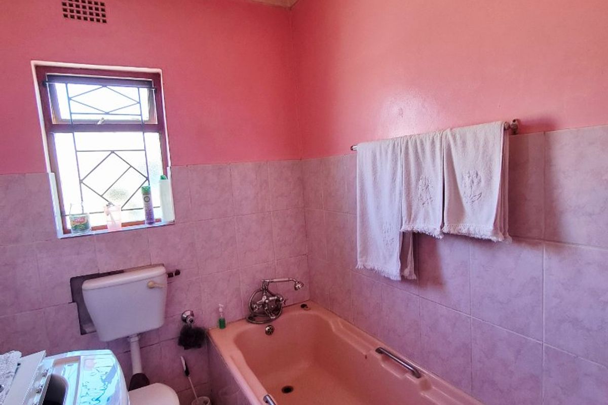 A dated bathroom featuring a pink bathtub, tiled walls, and a toilet. The space requires modernization to update the finishes and fixtures.