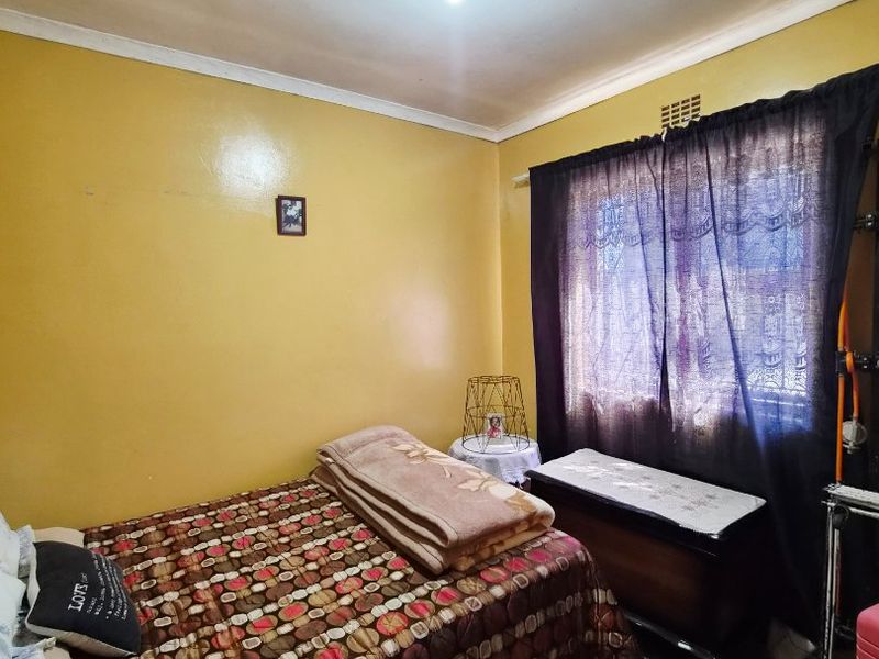 A bedroom featuring yellow painted walls, a ventilation grille, and a window with dark curtains.