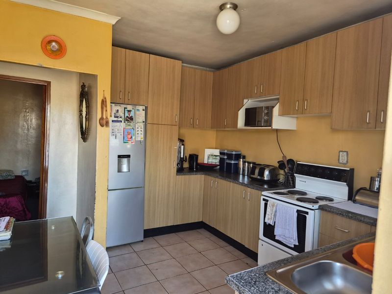 A functional kitchen featuring laminate cabinetry, stone-look countertops, and a freestanding electric stove, offering potential for modernization and aesthetic updates.