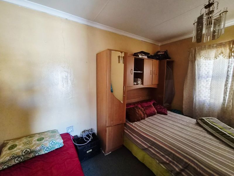 A bedroom featuring a built-in wardrobe and a ceiling light fixture, showing signs of wear including visible wall cracks.