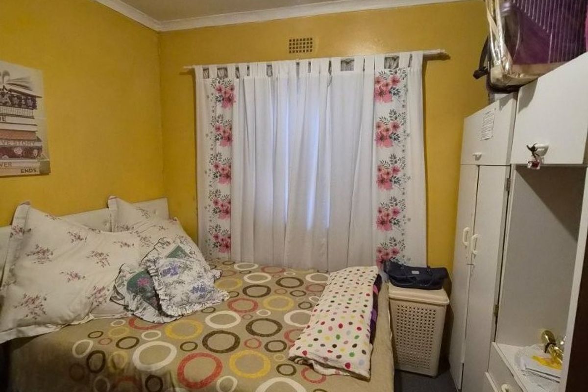 A compact bedroom featuring a built-in wardrobe and a ceiling ventilation vent, providing a functional sleeping space.