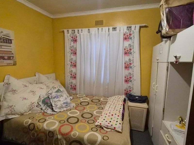 A compact bedroom featuring a built-in wardrobe and a ceiling ventilation vent, providing a functional sleeping space.