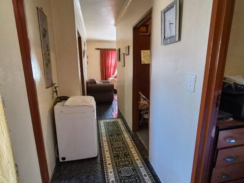 A narrow residential hallway featuring dark tiled flooring and access to multiple rooms, showing signs of wear and dated finishes.