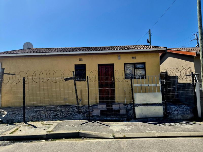 Front elevation of a single-story house featuring a tiled roof, security fencing with razor wire, and a paved entrance area.