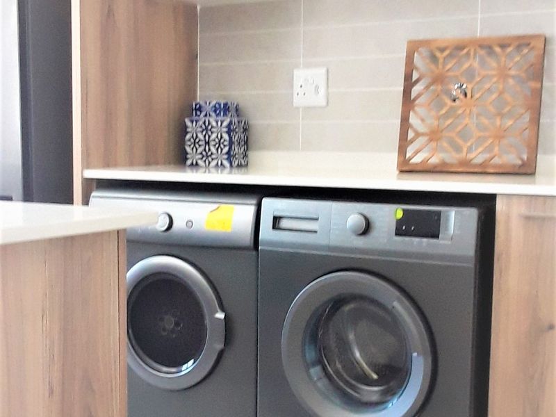 A modern laundry area featuring sleek dark cabinetry, stone countertops, and tiled backsplash, designed for efficient appliance integration.