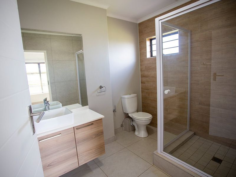 A modern, well-maintained bathroom featuring a floating vanity with a vessel sink, a glass-enclosed shower, and neutral floor-to-ceiling tiling.