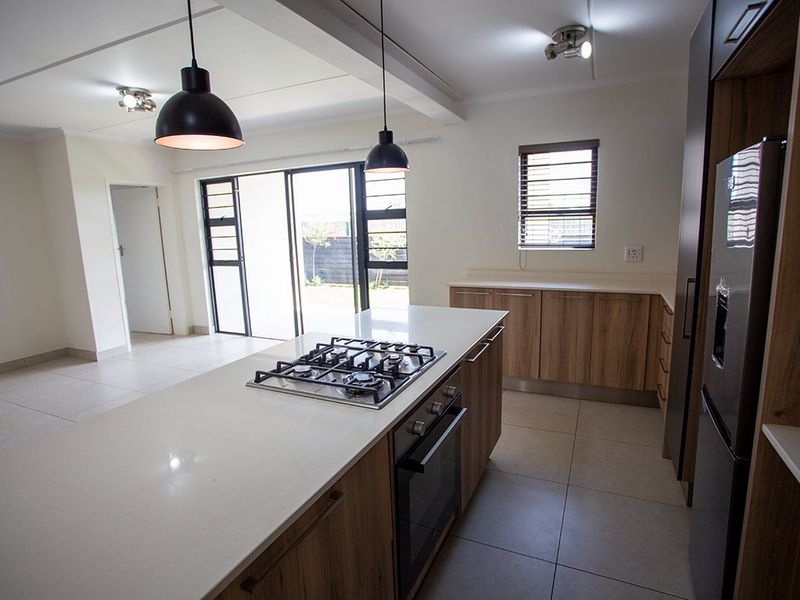 Modern open-plan kitchen featuring a central island with gas hob, built-in oven, stone countertops, and sleek cabinetry, flowing into a bright living area.