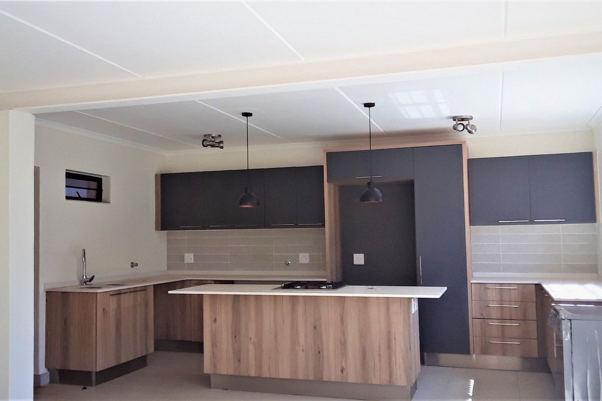 Modern kitchen featuring two-tone cabinetry, a central island with a built-in gas hob, tiled backsplash, and contemporary pendant lighting.