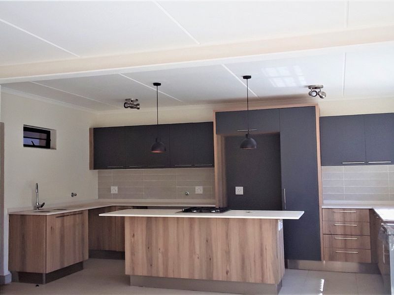 Modern kitchen featuring two-tone cabinetry, a central island with a built-in gas hob, tiled backsplash, and contemporary pendant lighting.