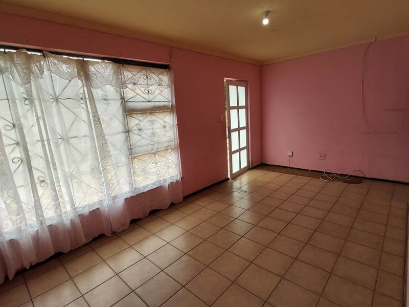 An empty living room featuring tiled flooring, a large window, and an external door, requiring cosmetic updates to the walls and finishes.