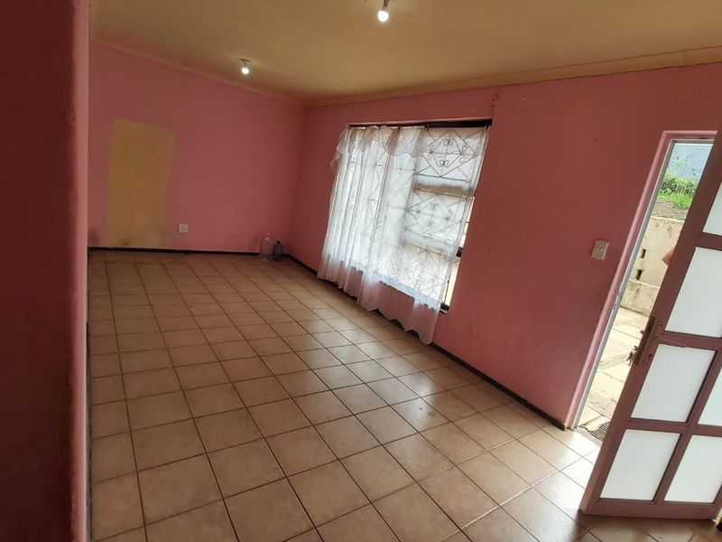 An empty living room featuring ceramic tiled flooring, pink walls, and a glass panel door leading to the exterior.