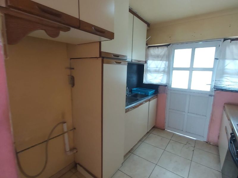 A functional kitchen space featuring built-in cabinetry, tiled flooring, and direct access to the exterior, offering potential for modernization and cosmetic updates.