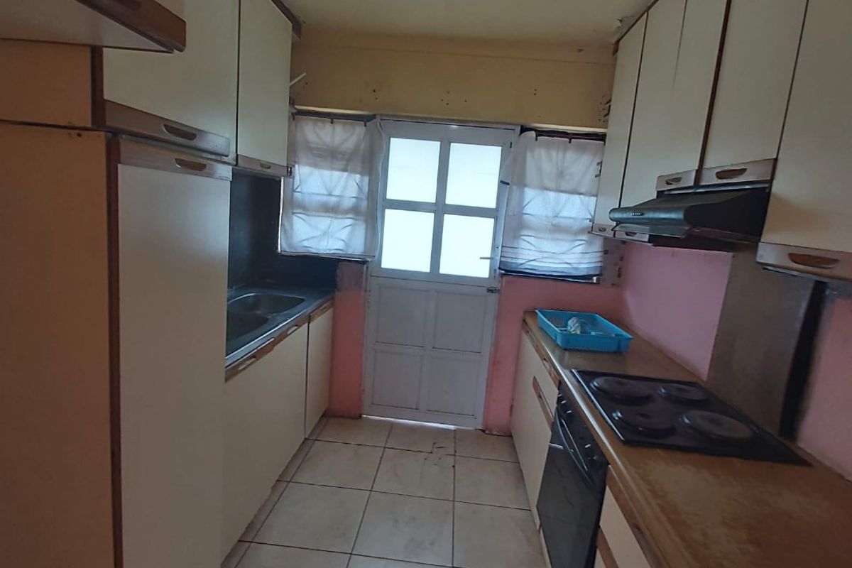 A compact kitchen featuring built-in cabinetry, an integrated oven with hob, and tiled flooring, offering a functional layout in need of cosmetic updates.