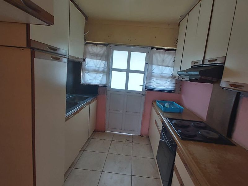 A compact kitchen featuring built-in cabinetry, an integrated oven with hob, and tiled flooring, offering a functional layout in need of cosmetic updates.