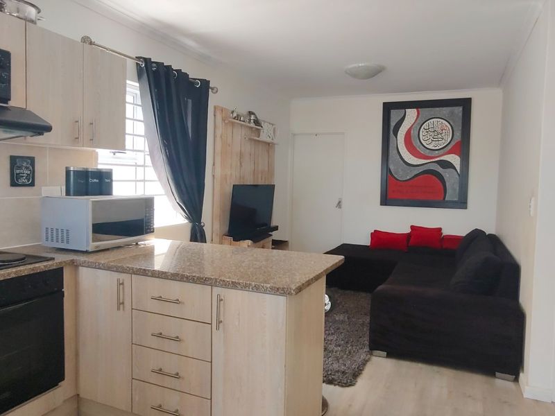 Open-plan kitchen and living area featuring light wood cabinetry, granite-look countertops, built-in appliances, and laminate flooring throughout.