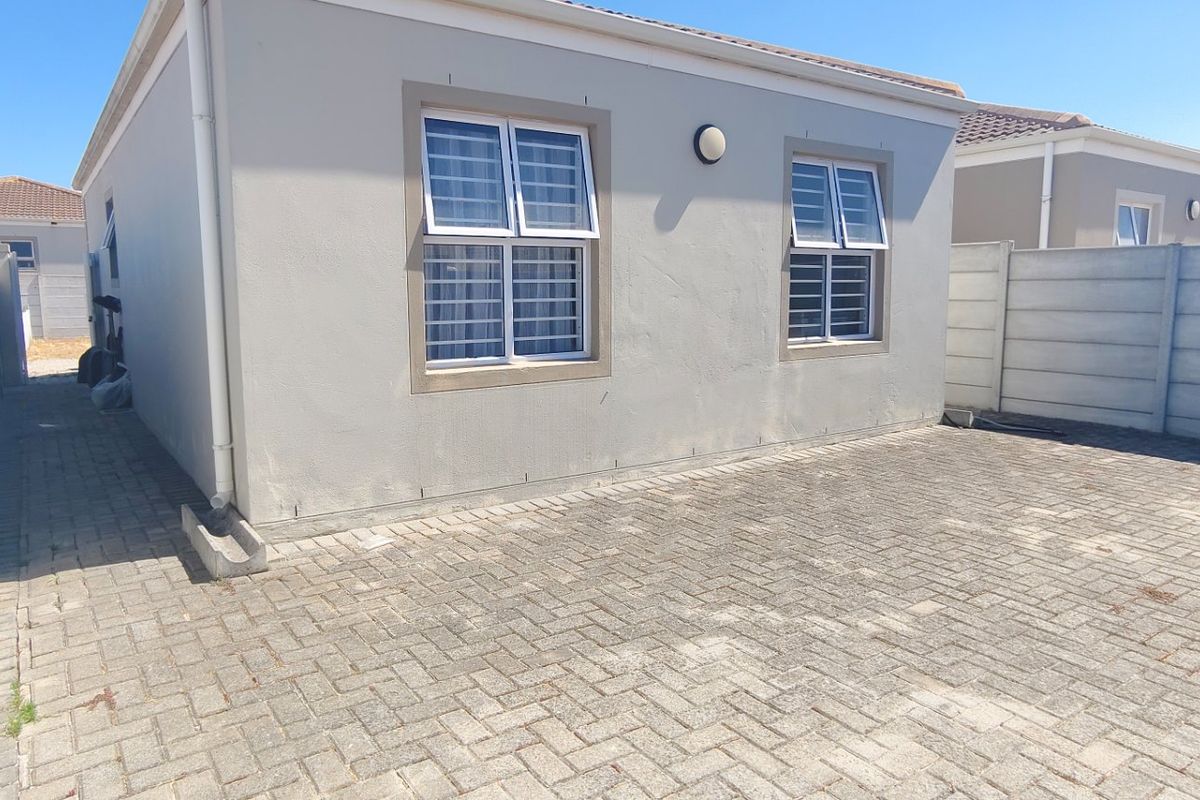 A rear exterior view of the property featuring a paved courtyard area, enclosed by precast concrete boundary walls and finished with neutral exterior paint.