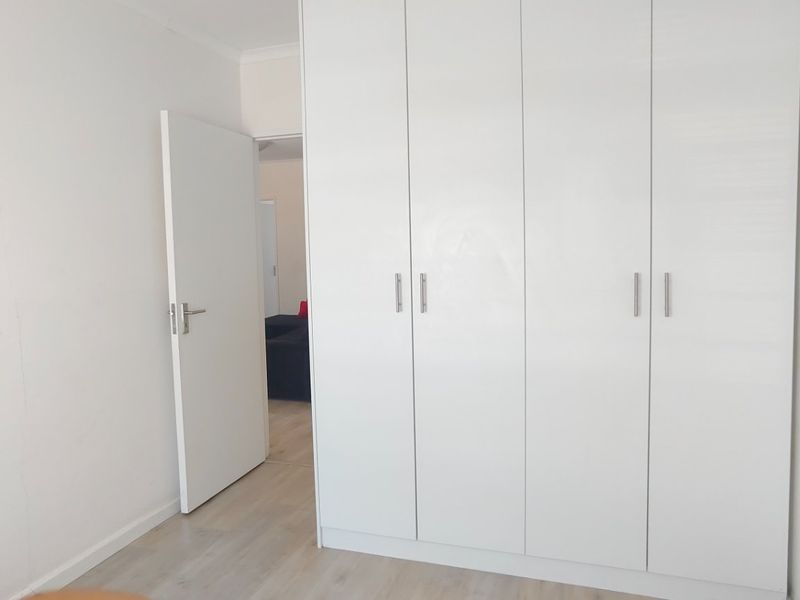 A clean, minimalist bedroom featuring light-toned laminate flooring and a large, white built-in wardrobe providing ample storage space.