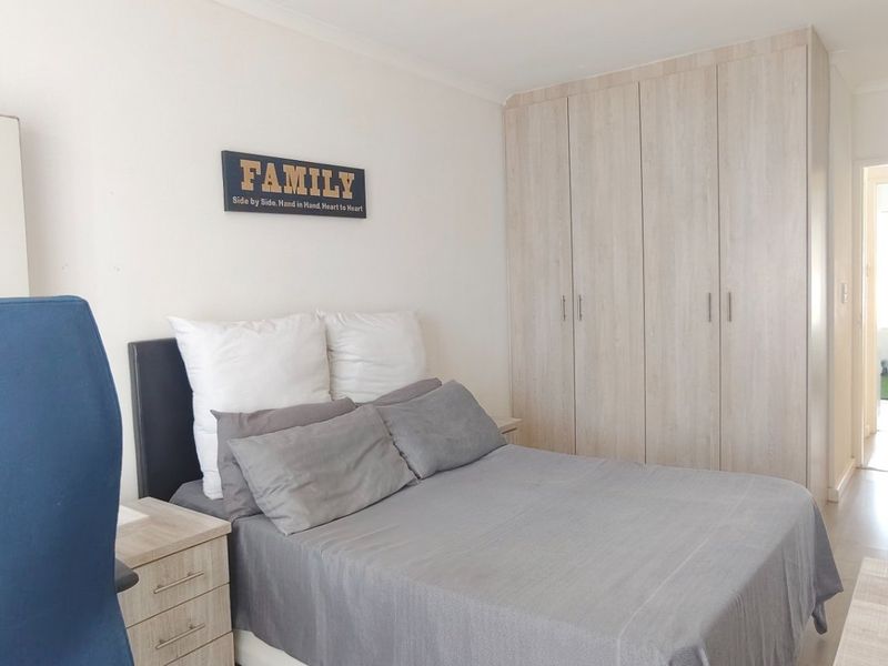 A functional bedroom featuring light-toned built-in cupboards and laminate flooring, offering a neutral base for personalization.