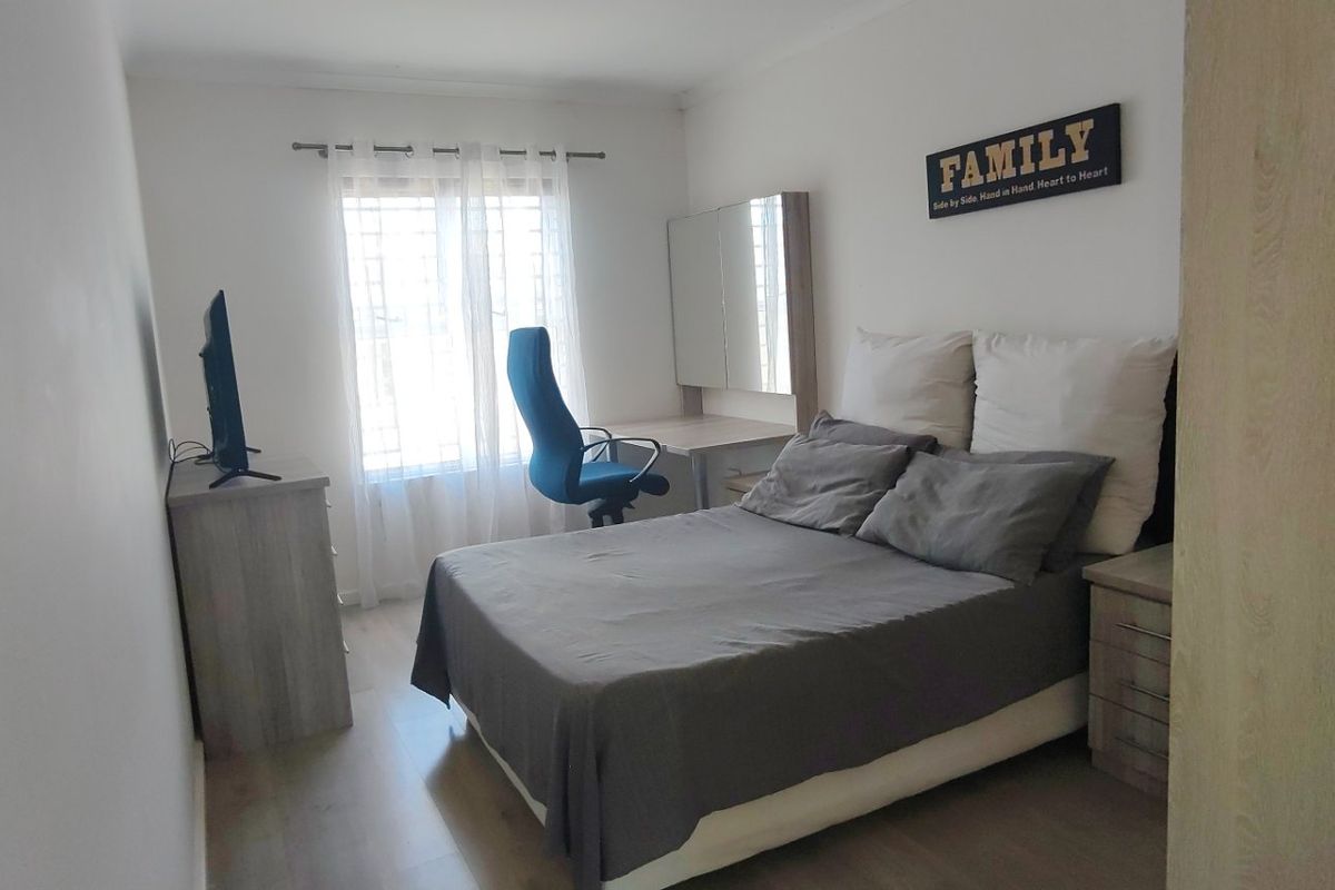A functional bedroom featuring laminate flooring, a built-in desk area, and a window fitted with security bars.