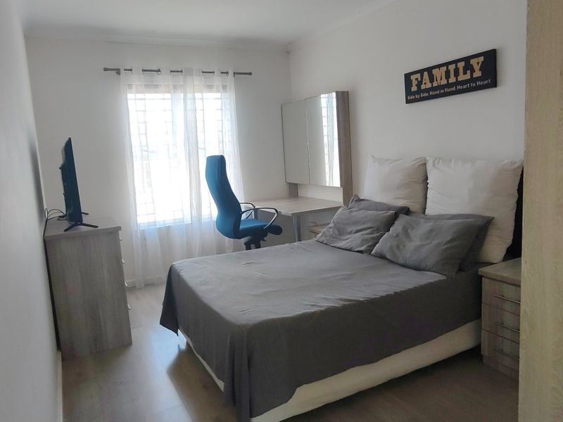A functional bedroom featuring laminate flooring, a built-in desk area, and a window fitted with security bars.