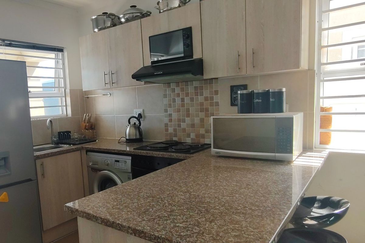 A functional kitchen featuring light wood cabinetry, granite countertops, a mosaic tile backsplash, and integrated appliances including a hob and extractor fan.