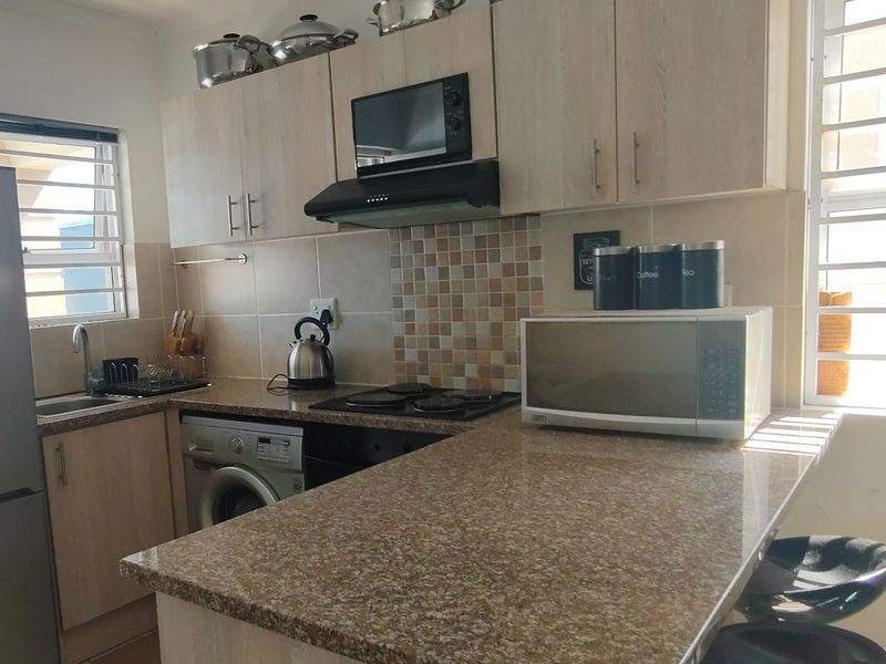 A functional kitchen featuring light wood cabinetry, granite countertops, a mosaic tile backsplash, and integrated appliances including a hob and extractor fan.