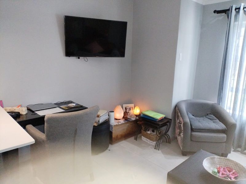 A living room area featuring tiled flooring and a wall-mounted television, offering a functional space for relaxation or home office use.