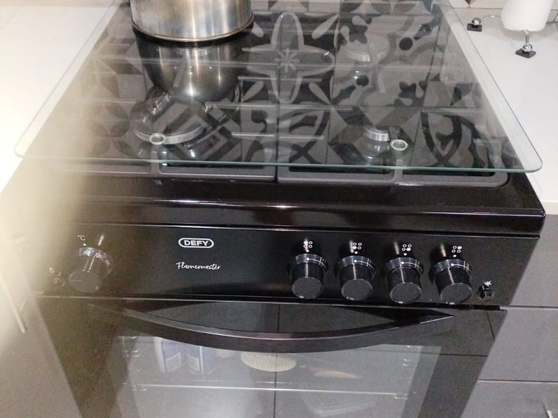 A modern kitchen featuring a black Defy Flamemaster oven and gas hob, complemented by a stylish patterned tile splashback and grey cabinetry.