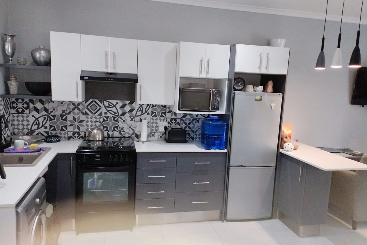 Modern kitchen featuring two-tone cabinetry, patterned tile backsplash, built-in oven with extractor fan, and an integrated breakfast bar with pendant lighting.