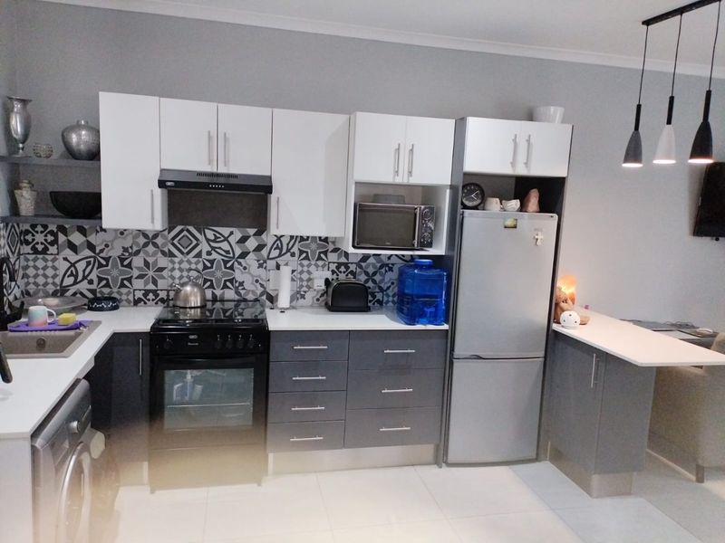 Modern kitchen featuring two-tone cabinetry, patterned tile backsplash, built-in oven with extractor fan, and an integrated breakfast bar with pendant lighting.