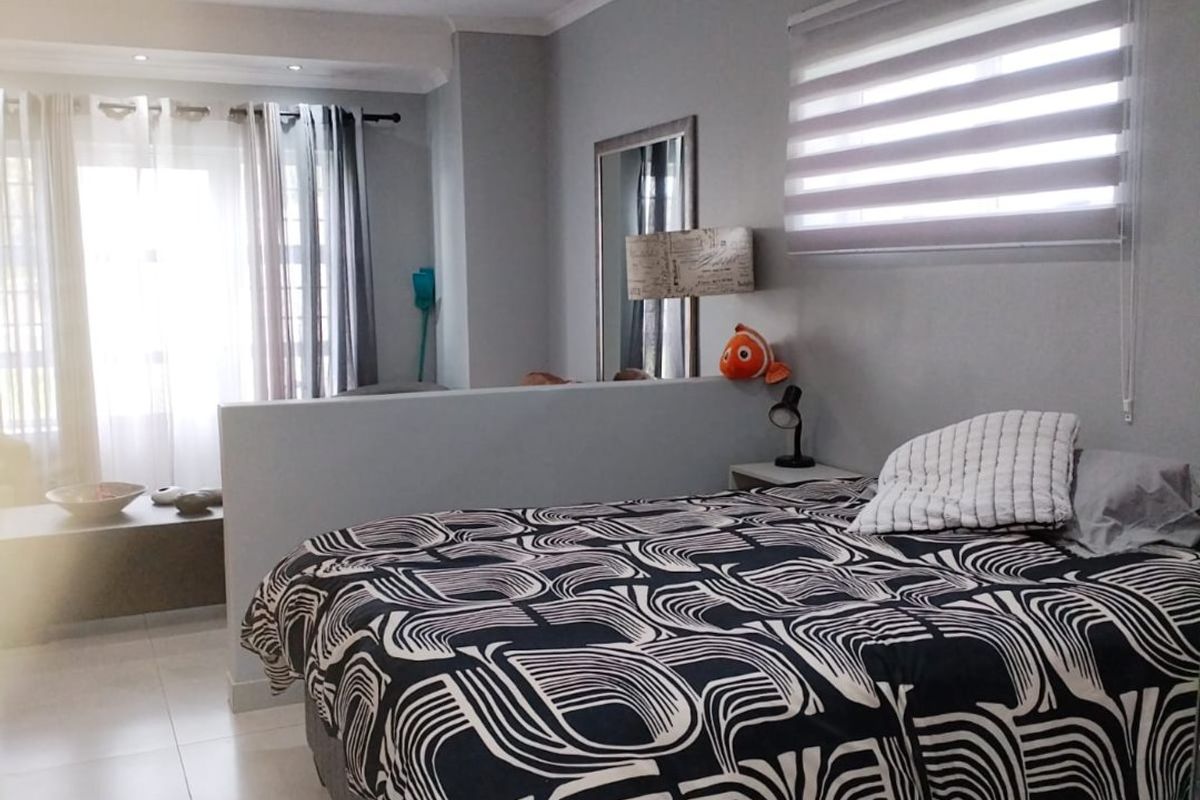 A well-maintained bedroom featuring tiled flooring, recessed downlighting, and a functional partition wall, with natural light provided by large windows with zebra blinds.