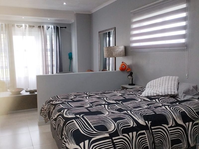 A well-maintained bedroom featuring tiled flooring, recessed downlighting, and a functional partition wall, with natural light provided by large windows with zebra blinds.