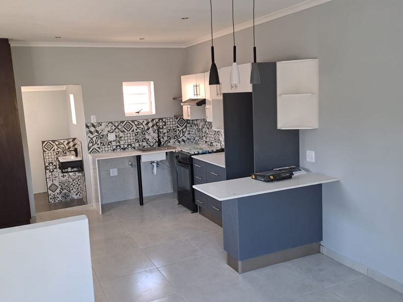 Modern kitchen featuring two-tone cabinetry, stone countertops, a striking patterned tile backsplash, and a breakfast bar, offering a clean and functional cooking space.
