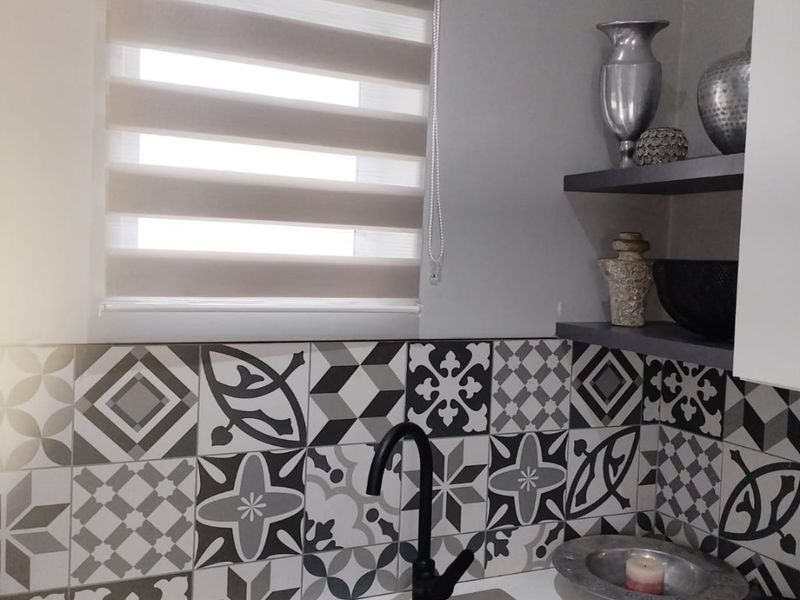 A modern kitchen corner featuring a composite sink with a black mixer tap, complemented by a stylish patterned tile splashback and floating shelving.