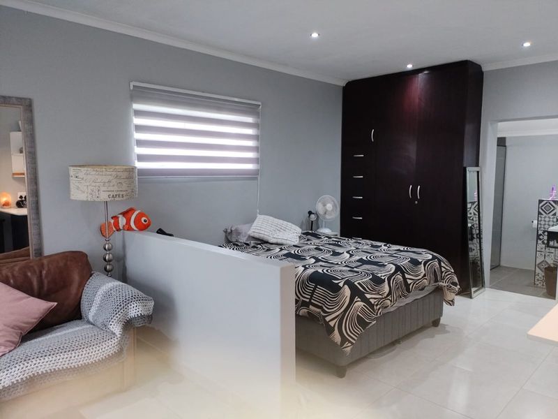 A well-maintained bedroom featuring built-in dark wood cupboards, modern tiled flooring, recessed downlighting, and a partial partition wall creating a distinct sleeping area.