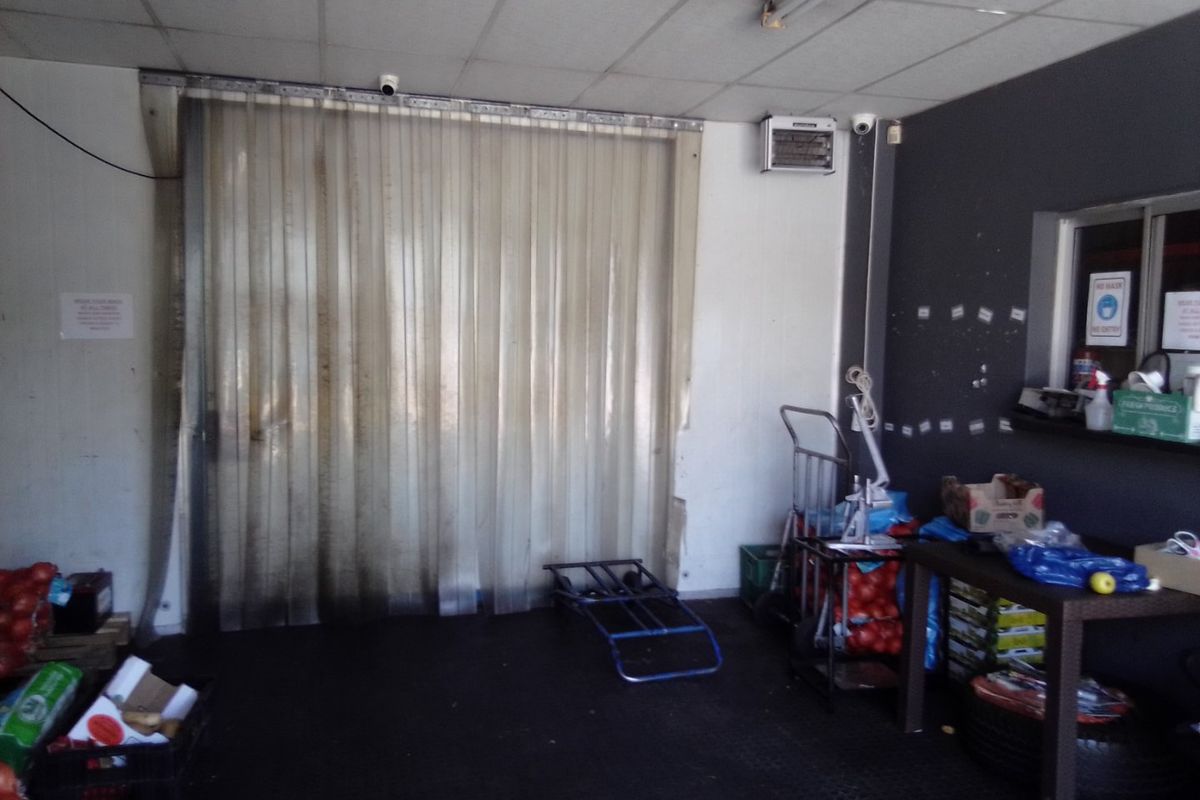 Commercial utility or storage area featuring a suspended ceiling, plastic strip curtain access, and a service window, showing signs of wear and heavy use.