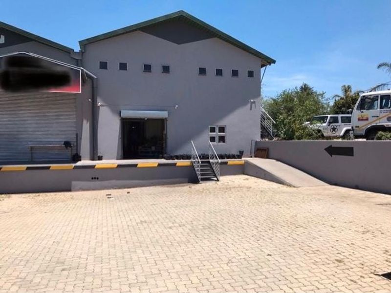 Commercial warehouse exterior featuring a paved loading yard, roller shutter door access, and a concrete loading dock with metal stairs.