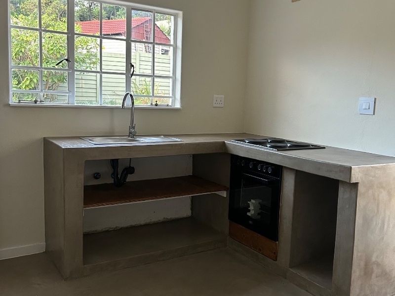 A minimalist kitchen featuring a concrete countertop, built-in oven and hob, and a stainless steel sink, currently awaiting final cabinetry finishes.