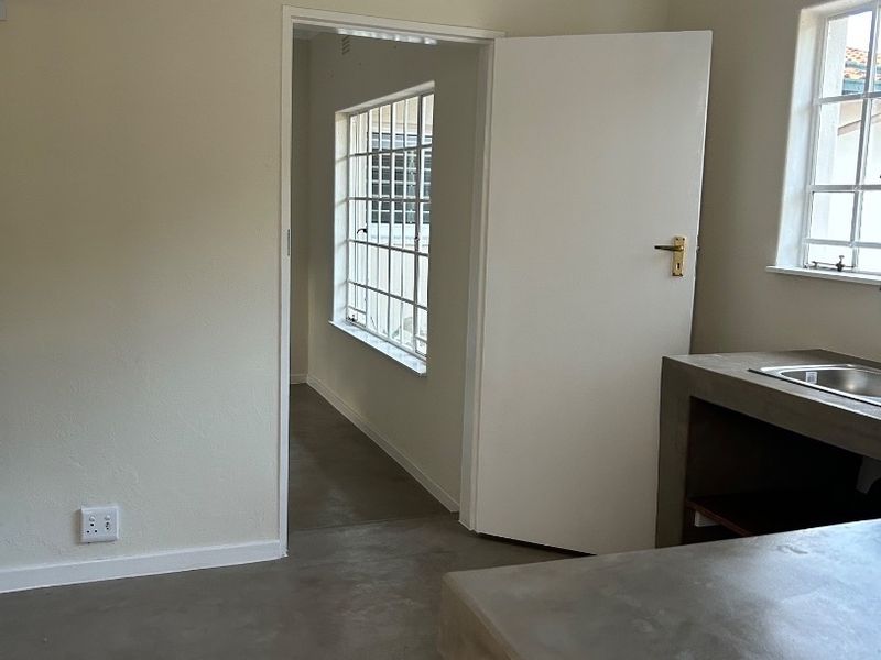 A minimalist kitchen area featuring concrete countertops, a stainless steel sink, and neutral walls, offering a clean, industrial-style foundation for customization.