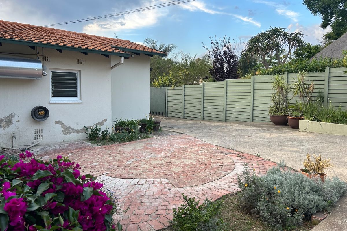 Rear exterior view of the property featuring a brick-paved patio area, concrete driveway, and perimeter timber fencing.