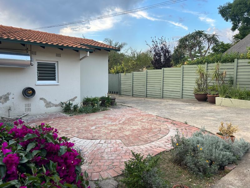 Rear exterior view of the property featuring a brick-paved patio area, concrete driveway, and perimeter timber fencing.