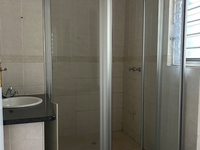 A functional bathroom featuring a corner shower enclosure, vanity basin with granite countertop, and tiled finishes throughout.