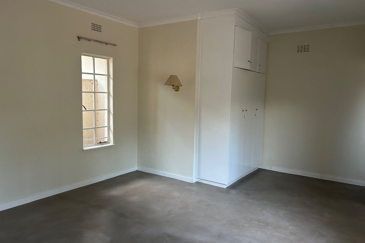 A spacious, empty bedroom featuring neutral walls, polished concrete flooring, and ample built-in cupboard storage.