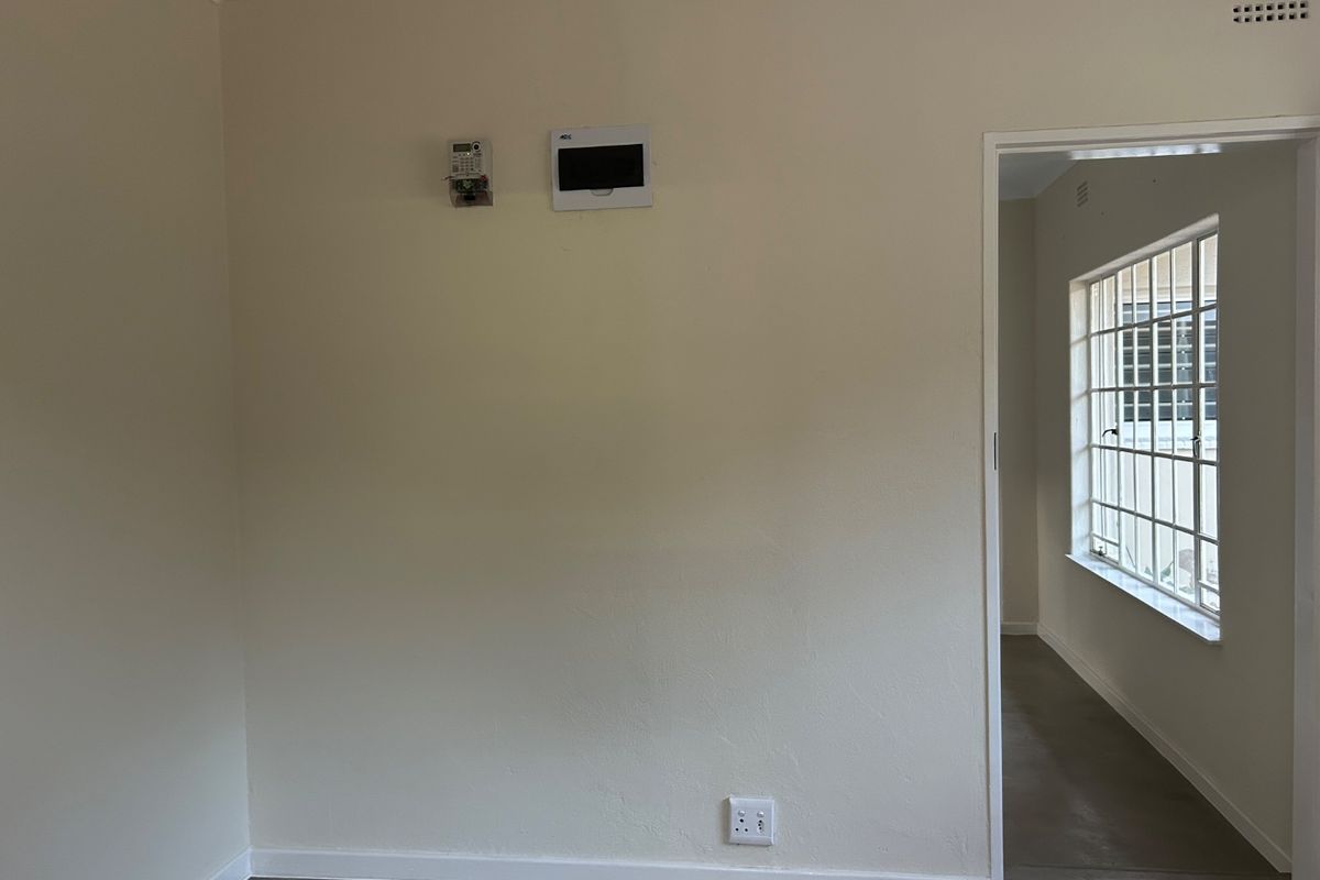 An empty living area featuring neutral walls, a prepaid electricity meter, a distribution board, and a steel-framed window with security bars.