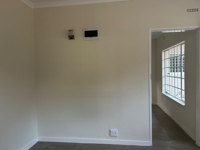 An empty living area featuring neutral walls, a prepaid electricity meter, a distribution board, and a steel-framed window with security bars.