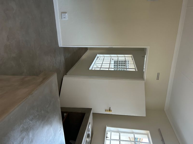 A minimalist kitchen area featuring polished concrete countertops, a built-in sink, and security-barred windows, offering a clean and functional space.