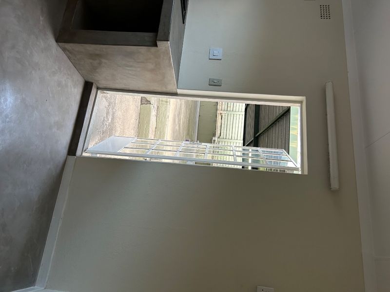 A minimalist kitchen area featuring a concrete countertop and built-in stove housing, with direct access to an outdoor patio area through a security gate.