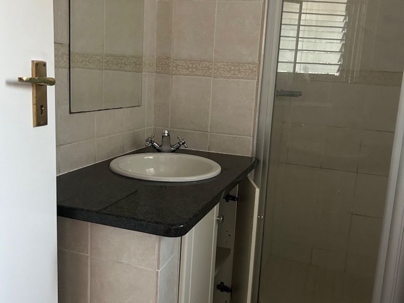 A compact bathroom featuring a vanity with an integrated sink, wall mirror, and a glass-enclosed shower with tiled finishes.