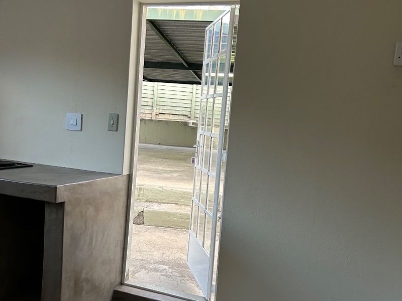 A minimalist kitchen area featuring a concrete countertop and cement flooring, with direct access to an outdoor patio through a glass paneled door.