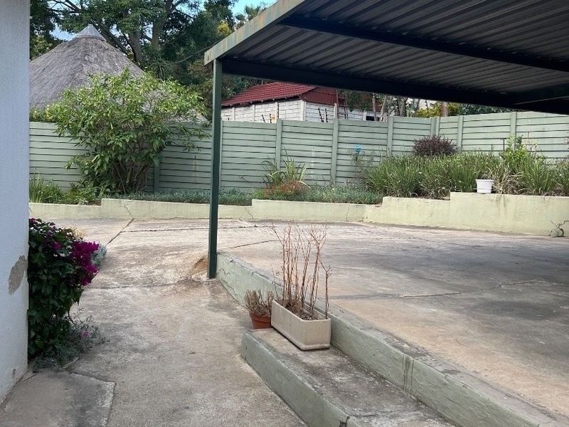 Rear exterior area featuring a covered carport, concrete paving, and a retaining wall with perimeter fencing.